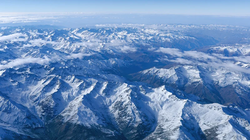 Aerial view of snow-covered mountain range with peaks and valleys under clear sky