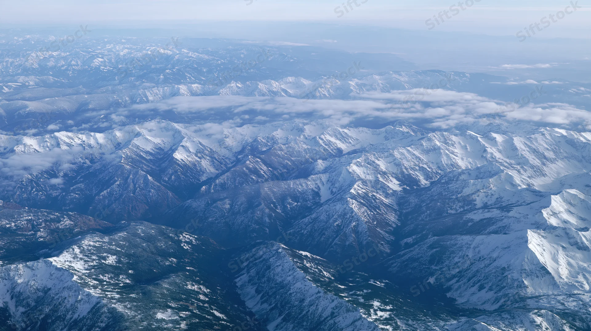 Aerial view of snow-covered mountain range from above with valleys and ridges stretching into the distance