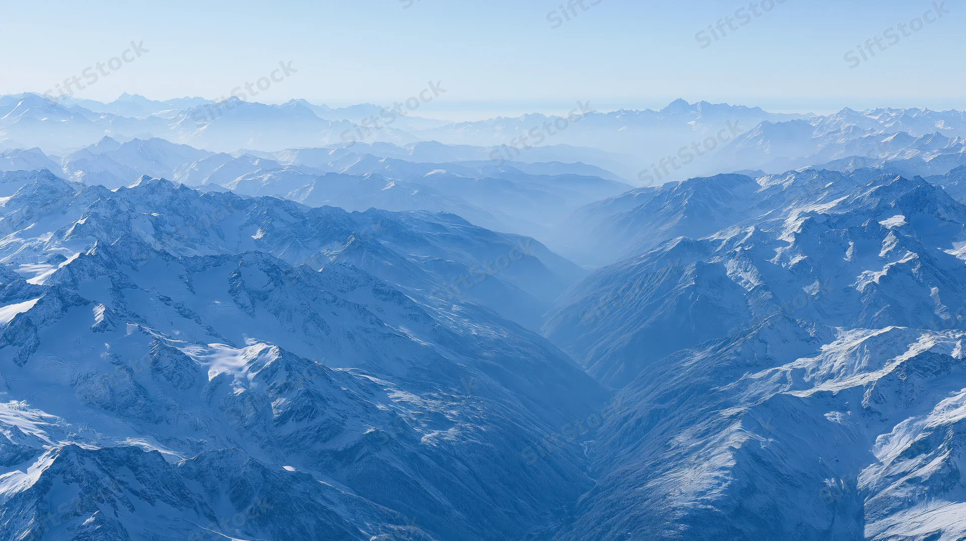 Aerial view of vast snow-covered mountain range stretching to the horizon under clear blue sky