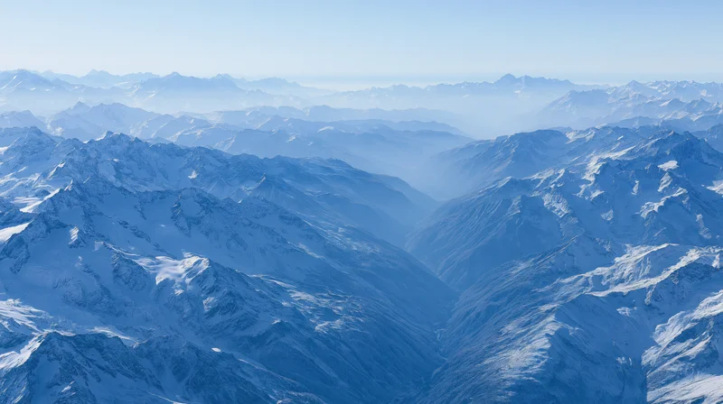 Aerial view of vast snow-covered mountain range stretching to the horizon under clear blue sky
