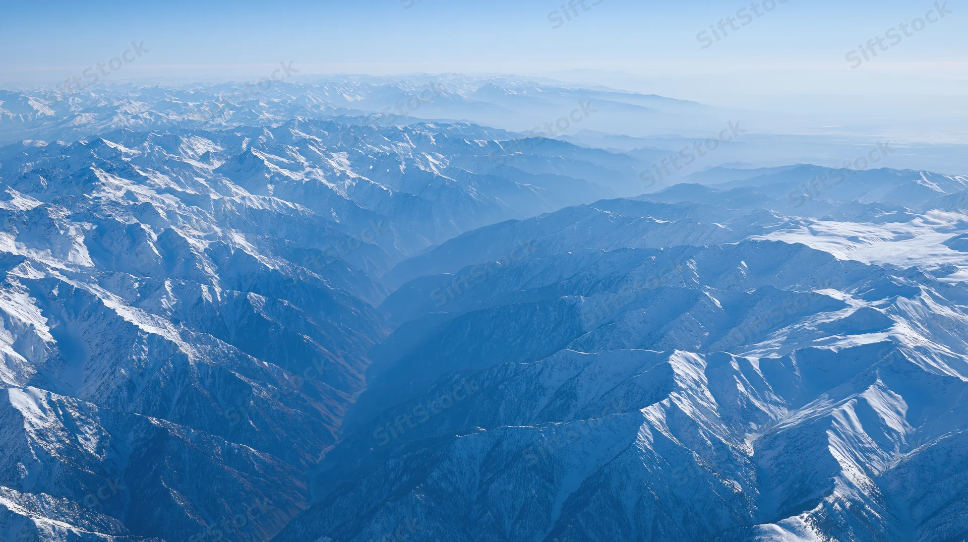 Aerial view of snow-covered mountain range stretching into the distance under clear blue sky