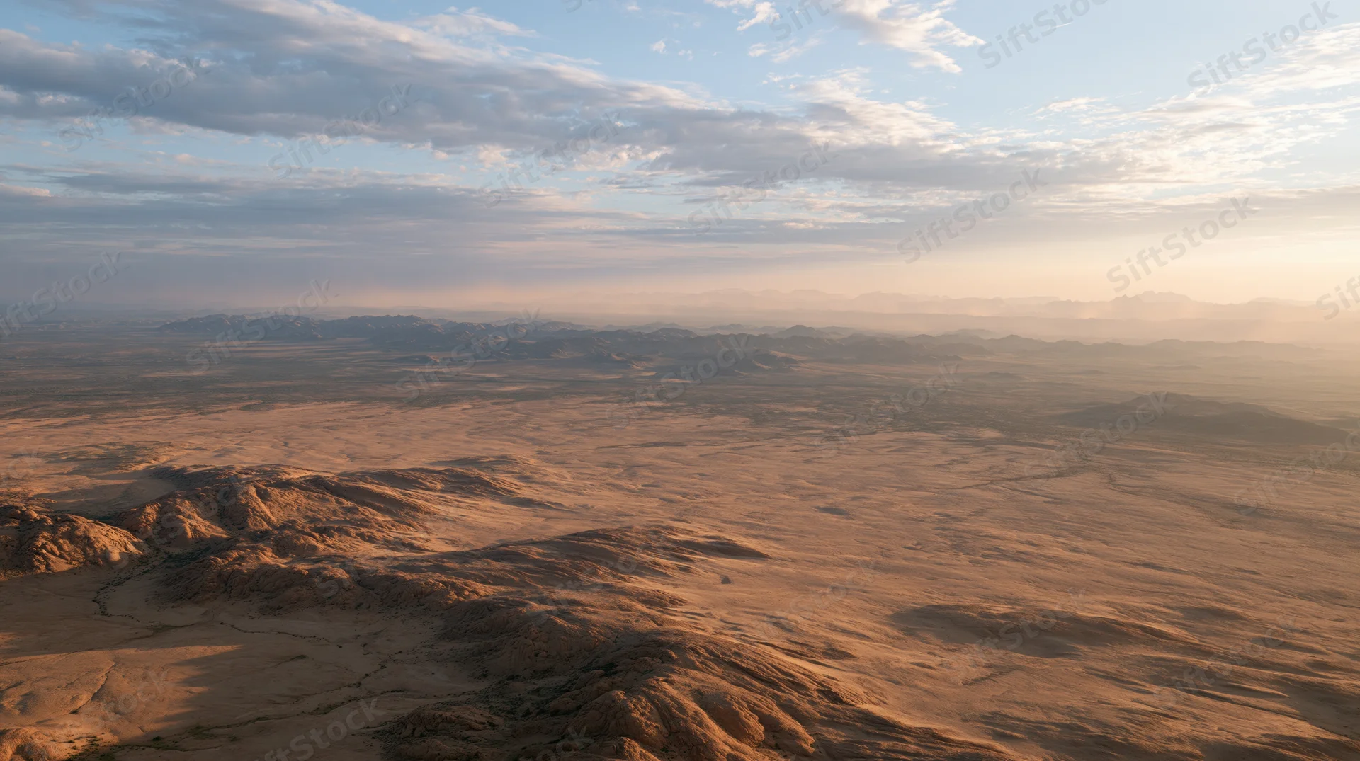 Aerial view of vast arid desert landscape stretching to distant mountains under hazy sky