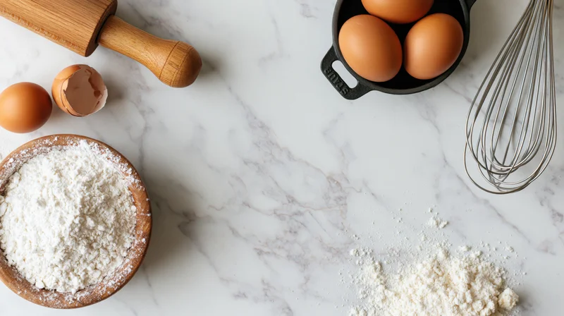 Baking ingredients arranged on a white marble countertop with wooden rolling pin and whisk