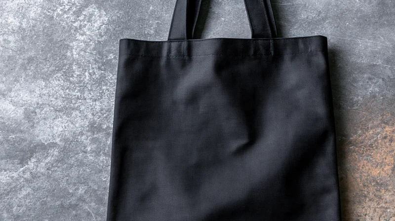 Black canvas tote bag lying flat on textured concrete surface with handles upright