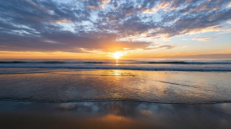 Sunset over calm ocean shoreline with gentle waves washing onto wet sand