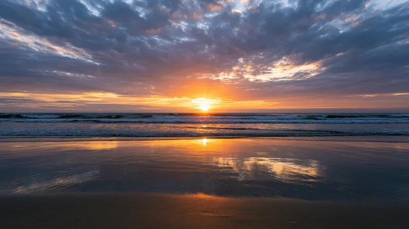 Sunset over calm ocean shoreline with gentle waves washing onto wet sand