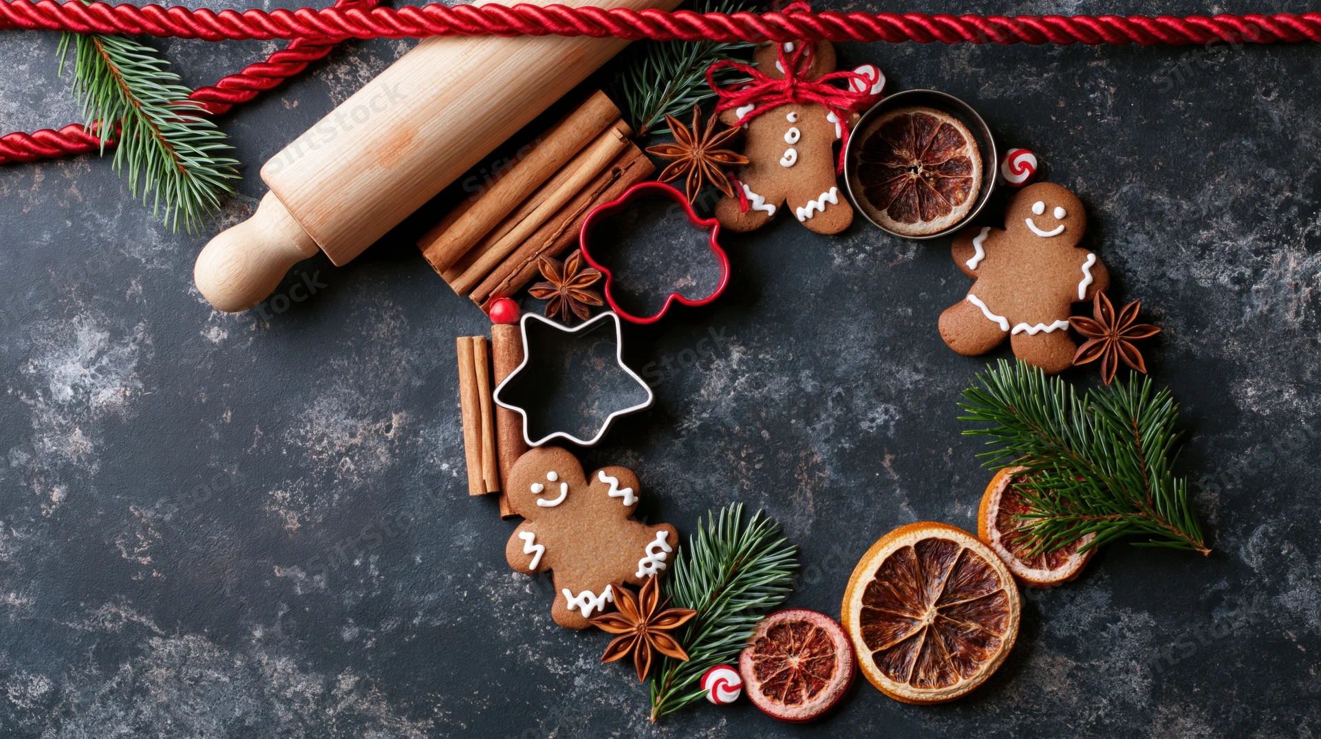 Gingerbread cookies and baking tools arranged in a festive flat lay on dark surface with pine and spices