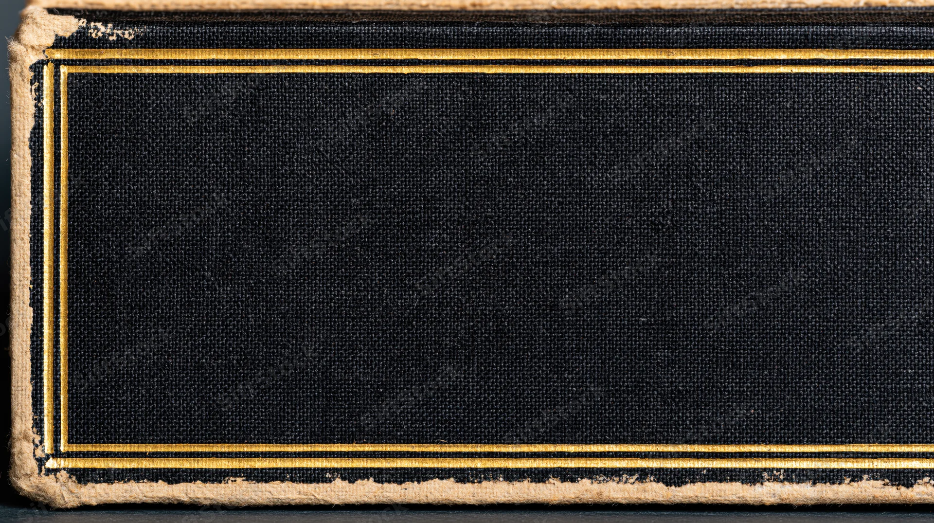 Close-up of an antique hardcover book cover with blank black fabric and gold trim, showing aged edges and texture
