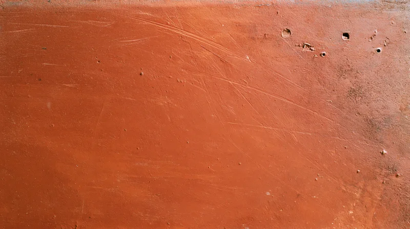 Close-up of a weathered reddish-brown painted metal surface with scratches and holes