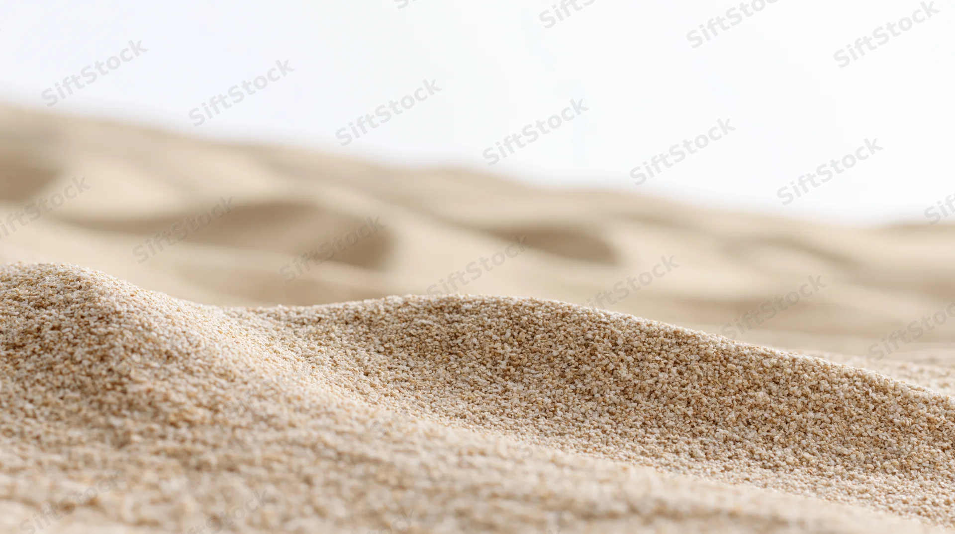 Close-up of dry beach sand with wind-formed ripples and soft texture against a bright background