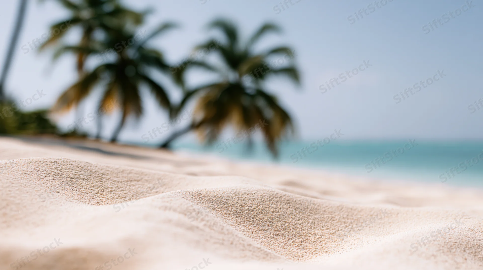 Close-up of smooth white sand with blurred palm trees and ocean in the background
