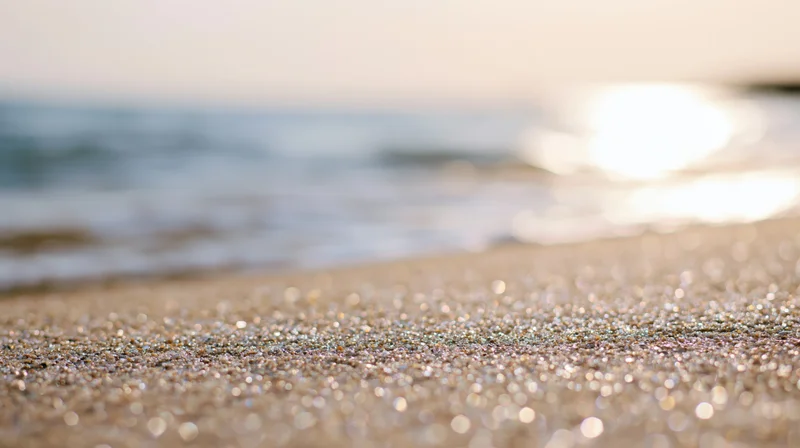 Closeup of wet sand sparkling in sunlight at beach shoreline with ocean waves in background