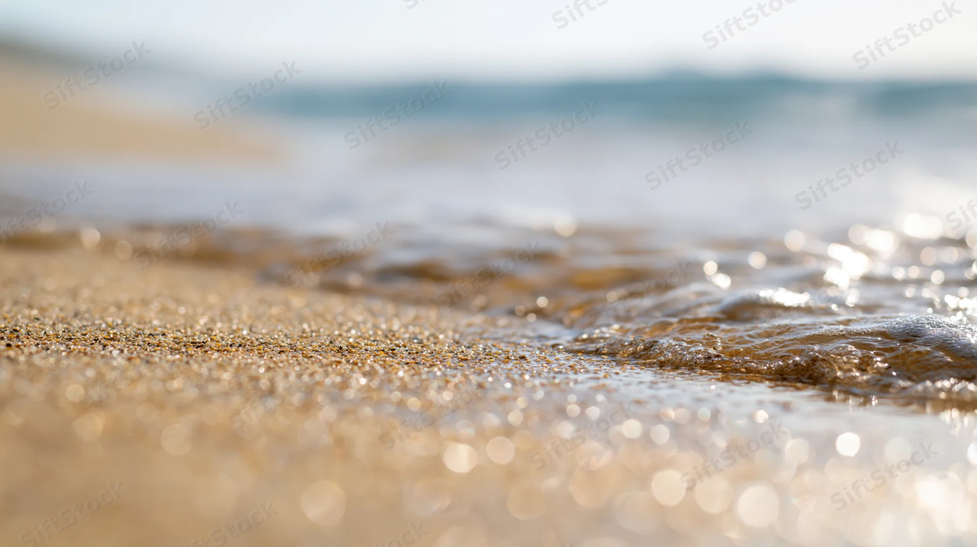 Close-up of wet sand at beach shoreline with gentle waves and sparkling sunlight