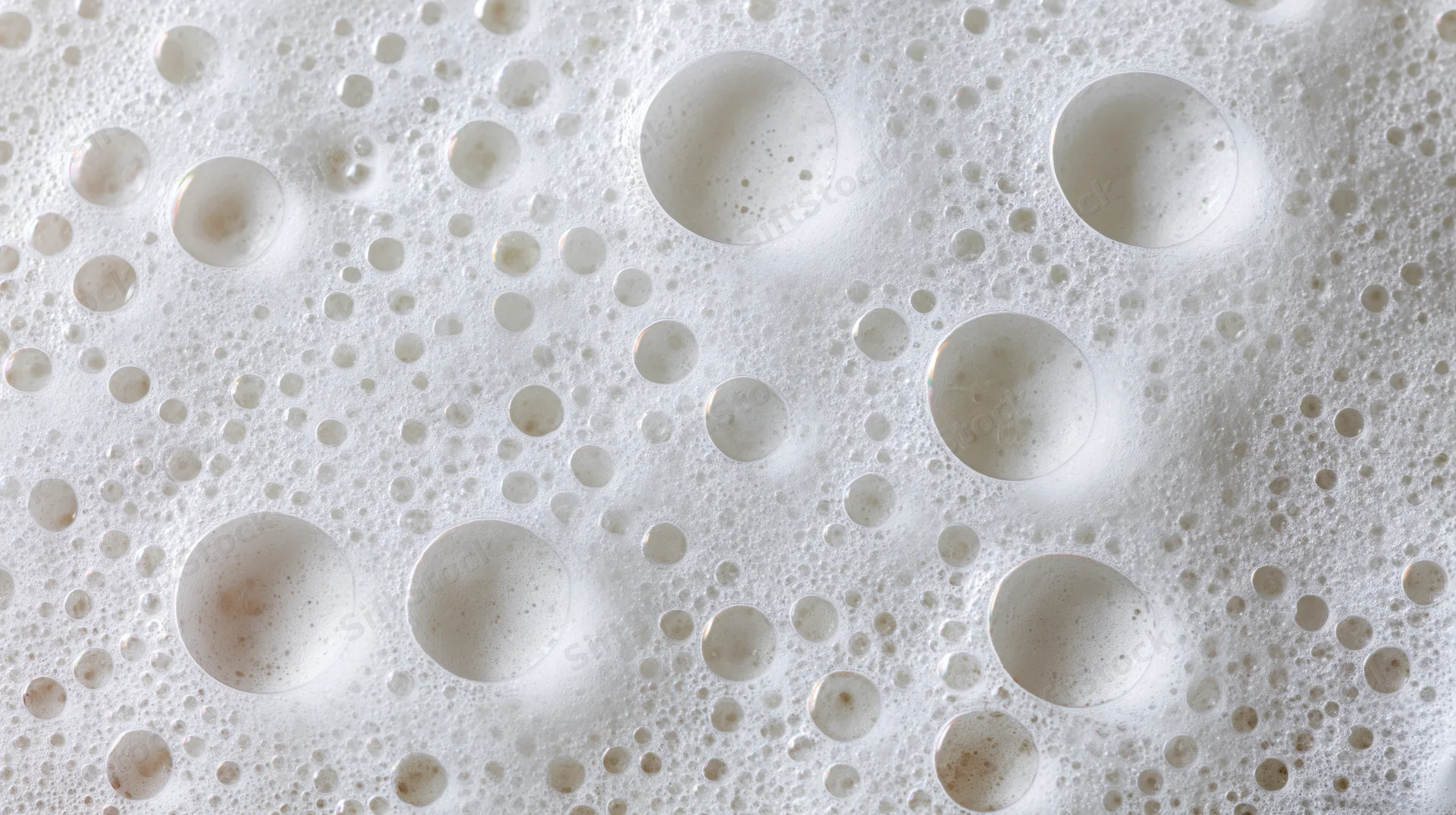Close-up overhead view of white soap foam surface with bubbles and circular patterns
