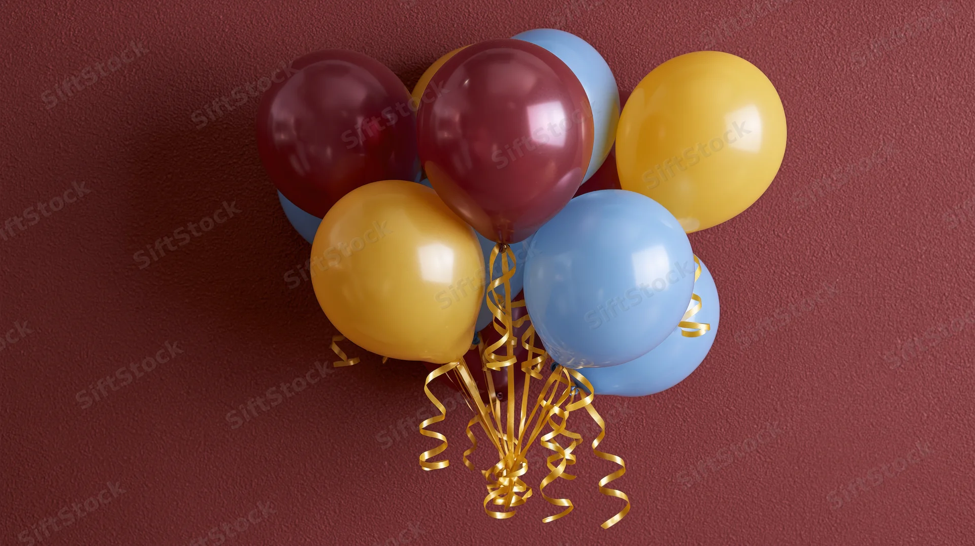 Cluster of burgundy yellow and sky blue latex balloons tied with gold ribbons against a red wall