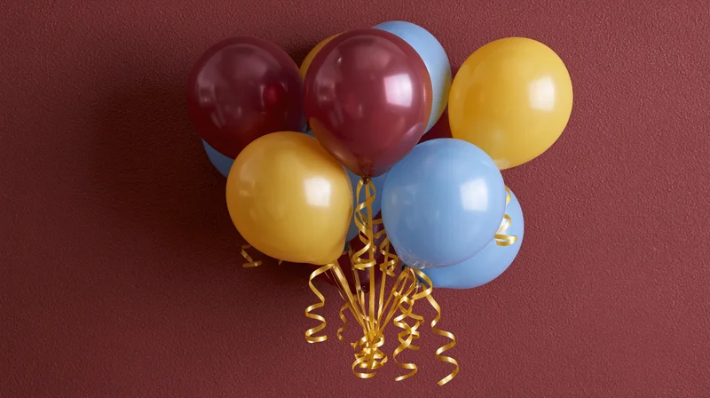 Cluster of burgundy yellow and sky blue latex balloons tied with gold ribbons against a red wall