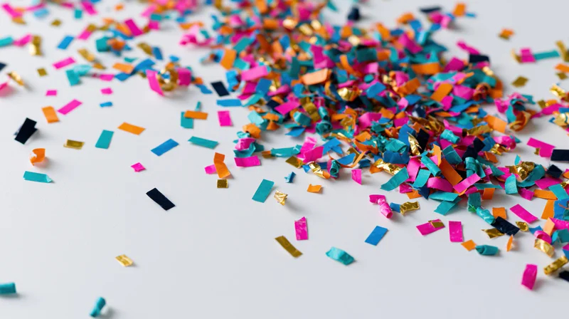 Colorful paper confetti scattered across a white surface in a flat lay view