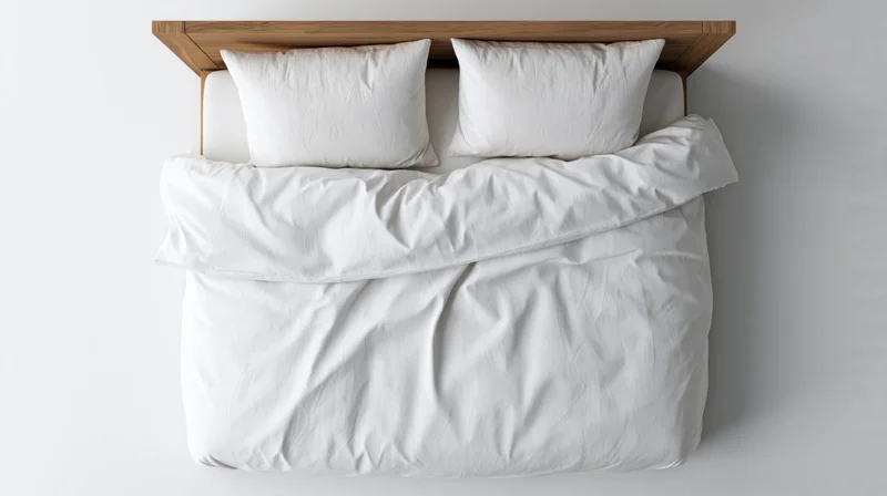 Overhead view of a double bed with white cotton duvet and two pillows against a plain wall