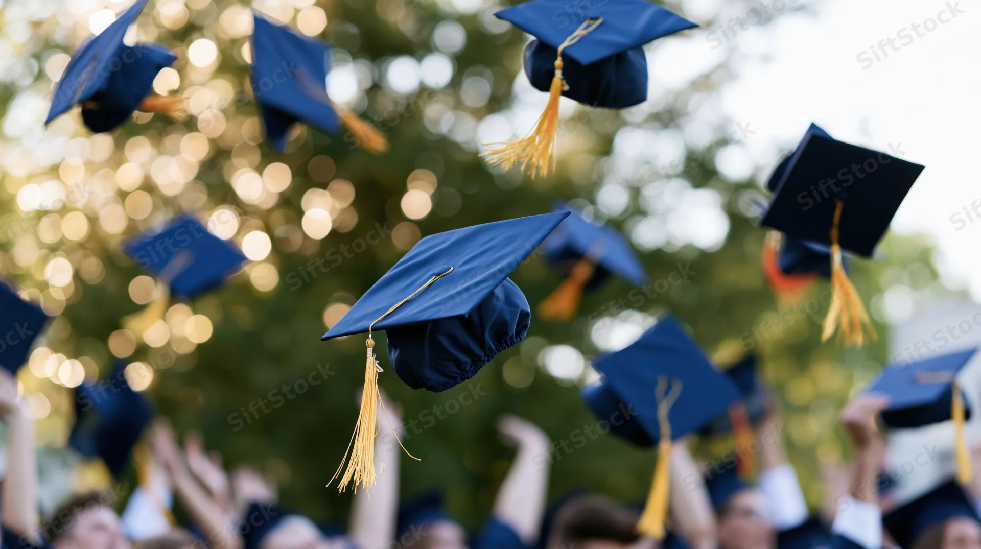 Navy blue graduation caps with gold tassels being thrown into the air at an outdoor ceremony