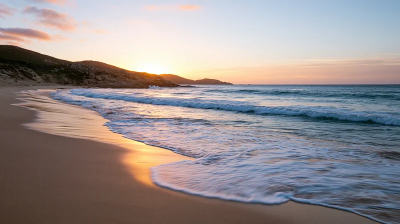 Gentle waves washing over sandy beach at sunset with cliffs and horizon in view