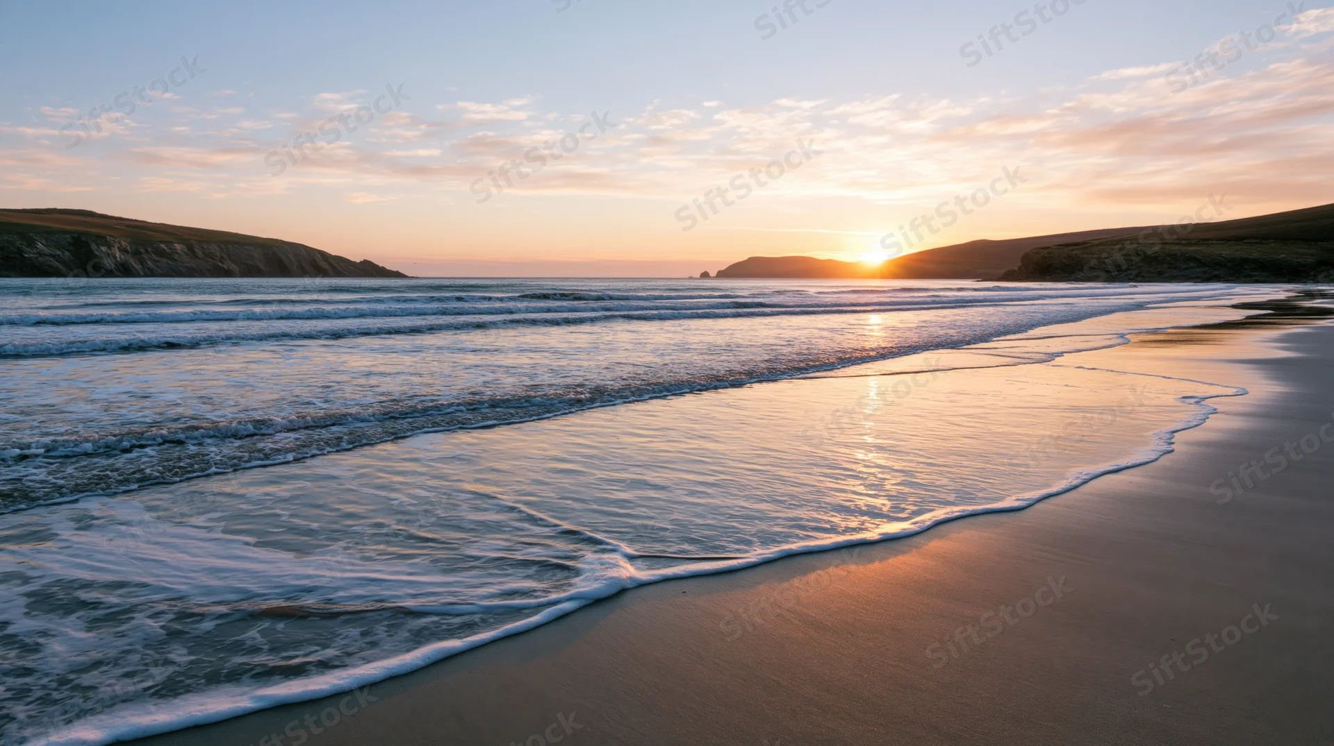 Gentle waves washing over sandy beach at sunset with cliffs on horizon