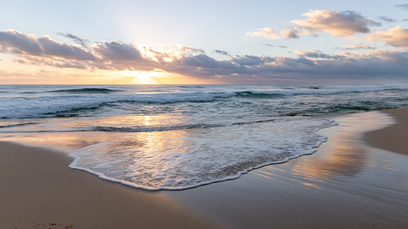Gentle waves washing onto sandy beach at sunrise with sky reflection