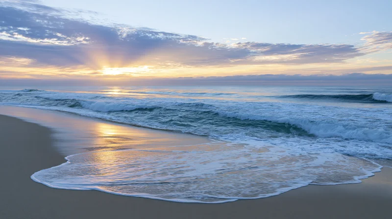 Gentle waves washing onto sandy beach at sunrise with golden light reflecting on wet sand and sky