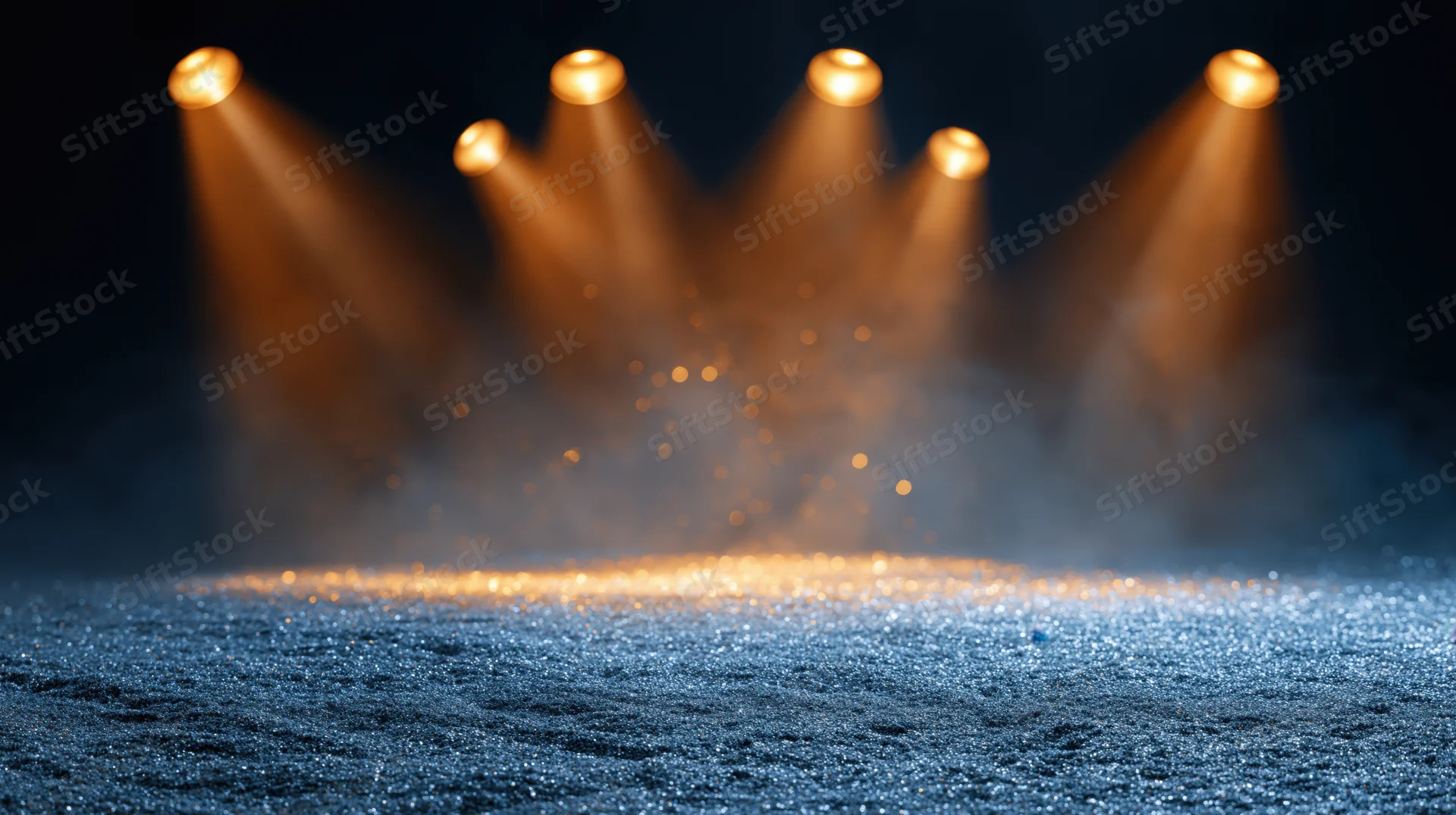 Empty stage floor covered in blue glitter under warm spotlights with haze