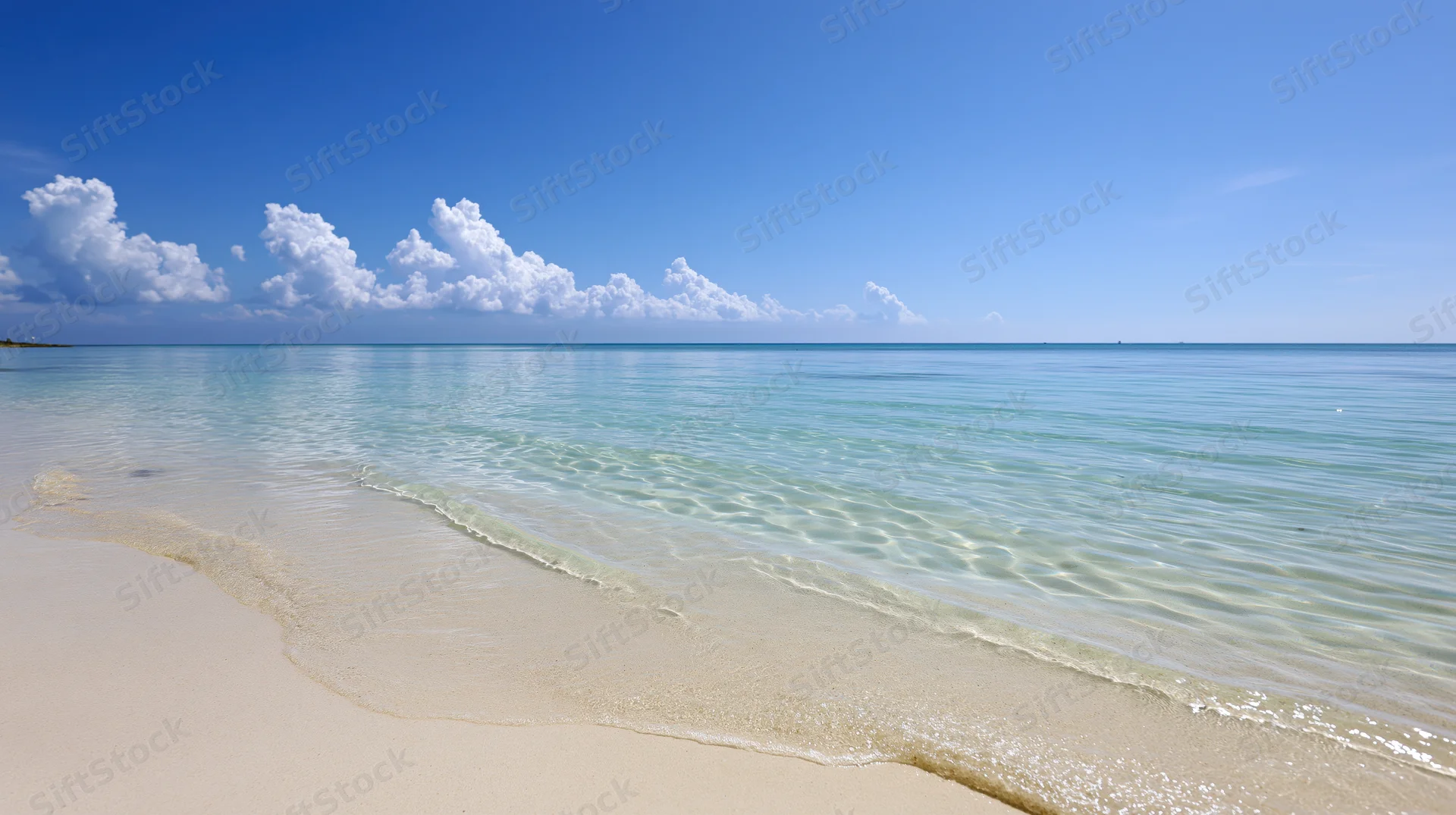Calm turquoise water lapping onto white sand beach under blue sky with clouds