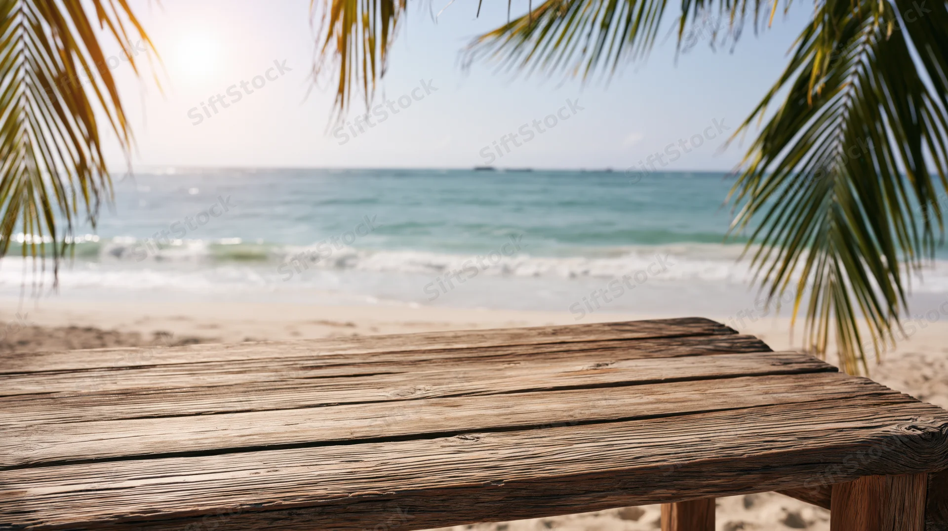 Weathered wooden table on sandy beach with ocean and palm fronds in background