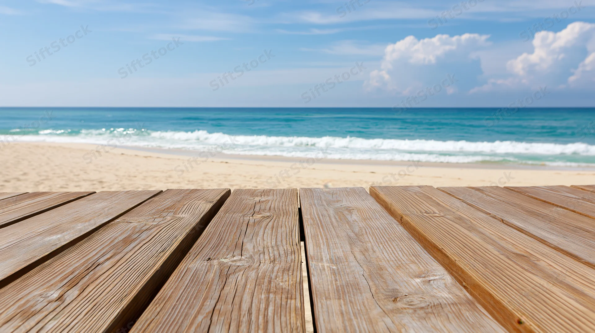 Wooden deck planks leading to a sandy beach with ocean waves and blue sky in the background