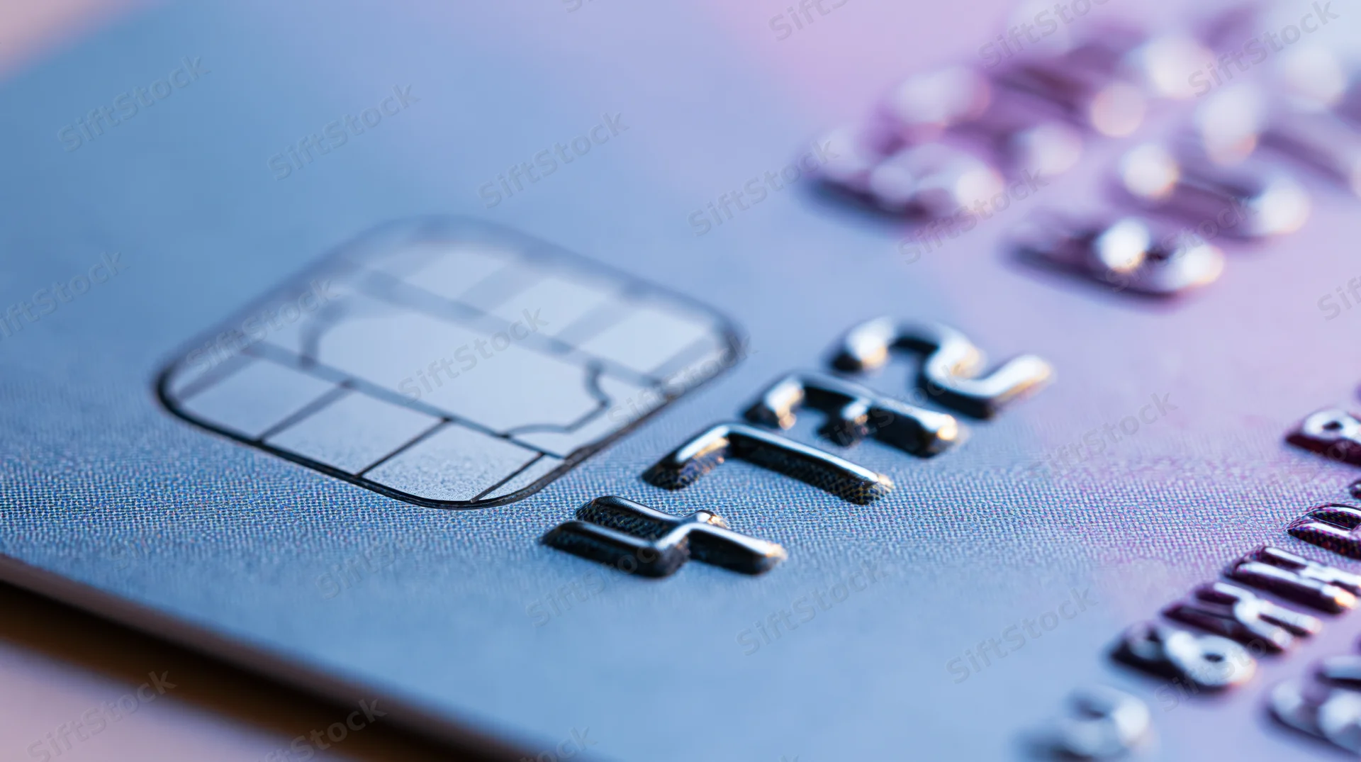 Close-up of a credit card showing the emv chip and embossed numbers on a blue plastic surface