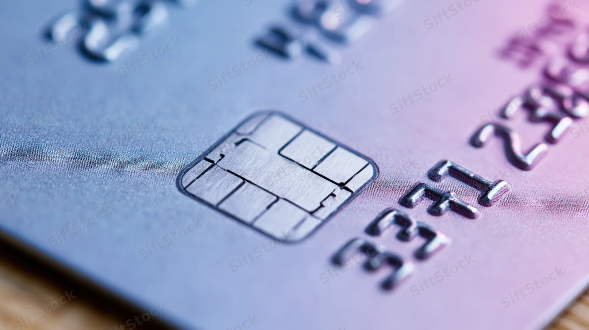 Close-up of a credit card showing the emv chip and embossed numbers on a gradient surface