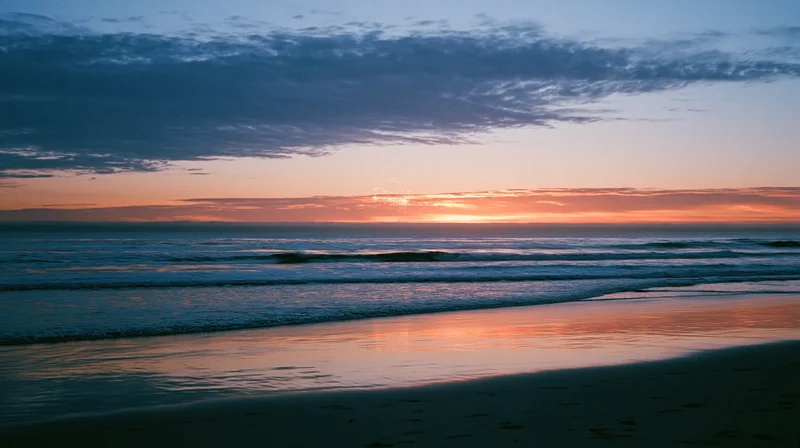 Twilight ocean horizon with waves rolling onto sandy beach under cloudy sky
