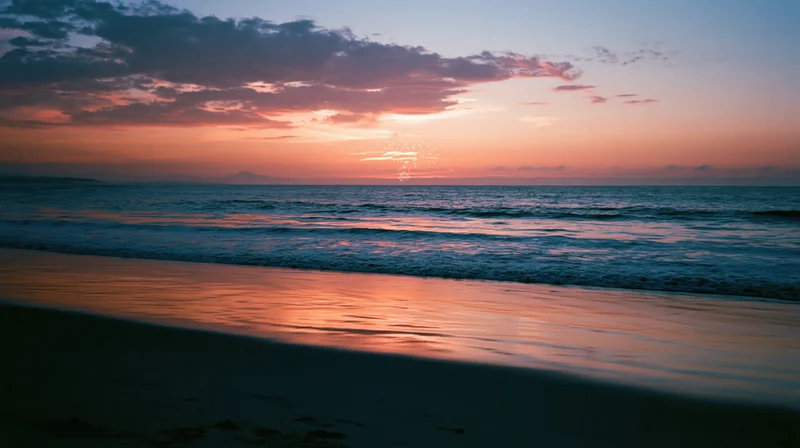 Sunset over calm ocean with pink and orange sky reflecting on water and wet sand at twilight