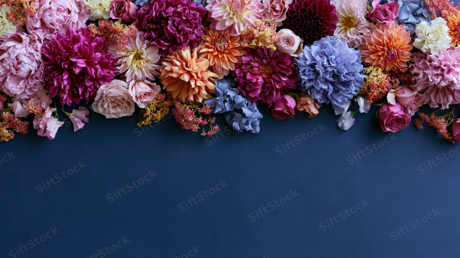Colorful mixed garden flowers arranged in a flat lay along the top of a navy blue surface with copyspace below
