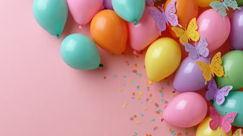 Colorful party balloons and paper butterflies arranged on pink surface with confetti and copyspace