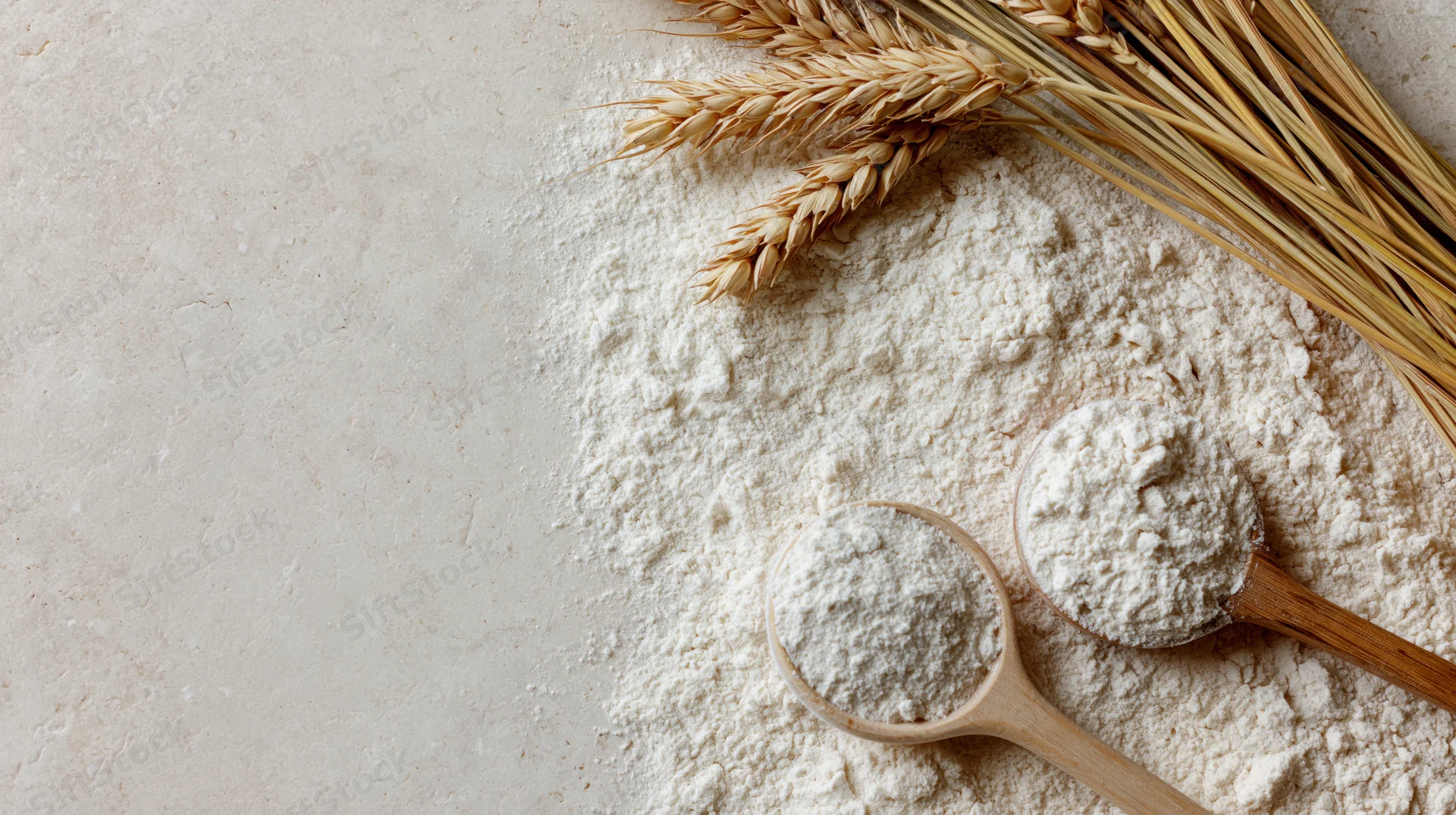 Scattered flour with wheat stalks and wooden spoons on a cream surface