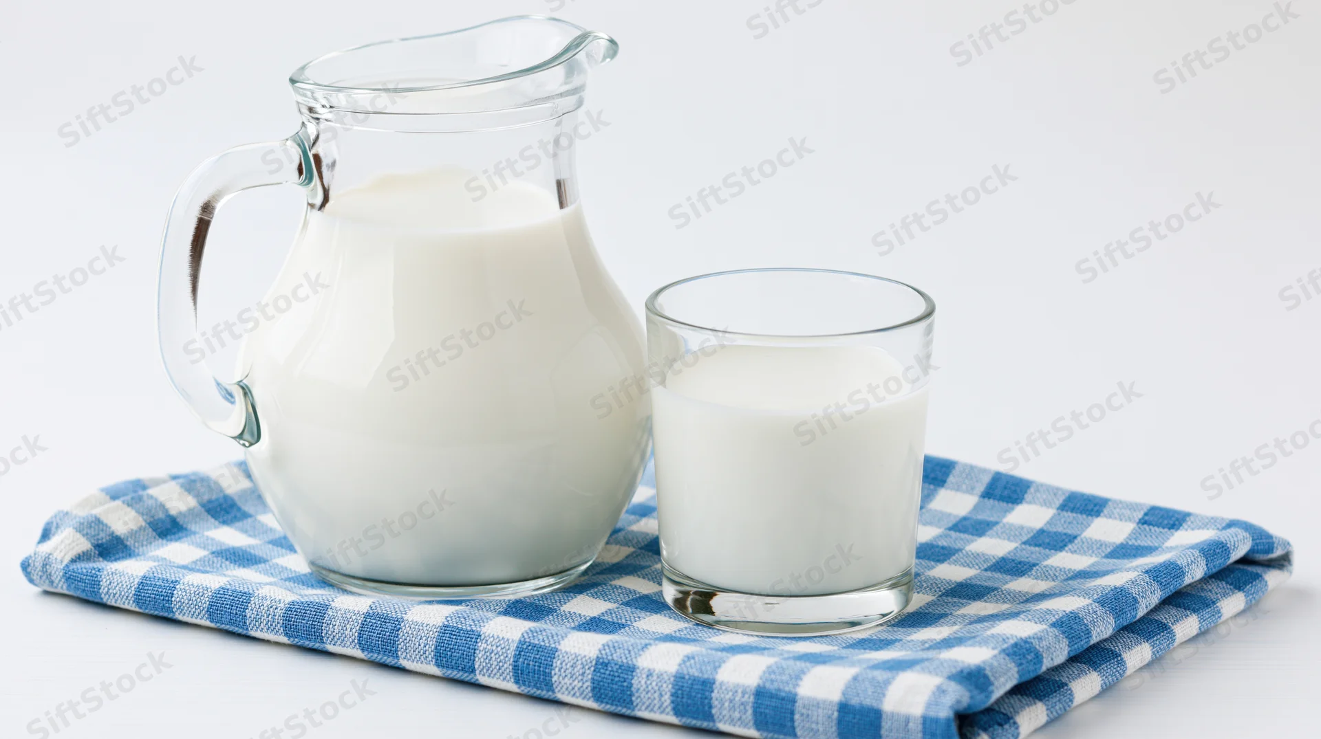 Glass pitcher and tumbler filled with milk on a blue checkered cloth
