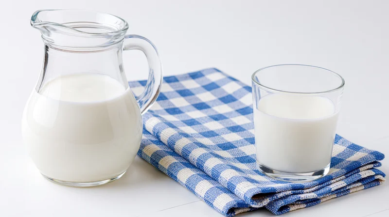 Glass pitcher and tumbler filled with milk on a checkered cloth on a white surface