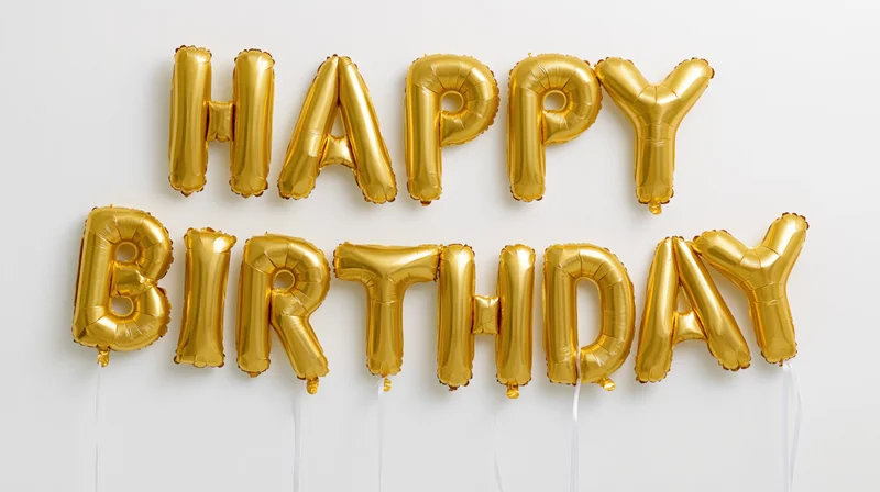 Gold foil letter balloons spelling happy birthday in two rows against white background