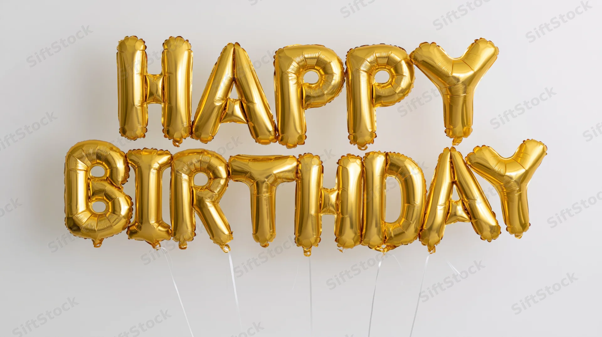Gold foil letter balloons spelling happy birthday in two rows against white background