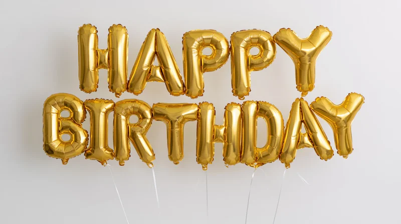 Gold foil letter balloons spelling happy birthday in two rows against white background