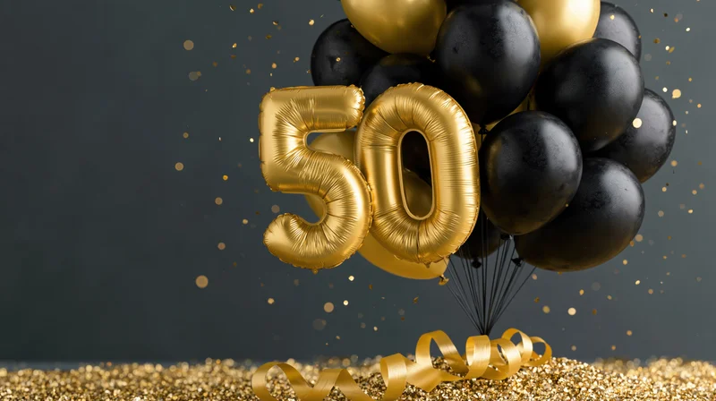 Gold foil number 50 balloons tied with black ribbons on glittery surface with confetti