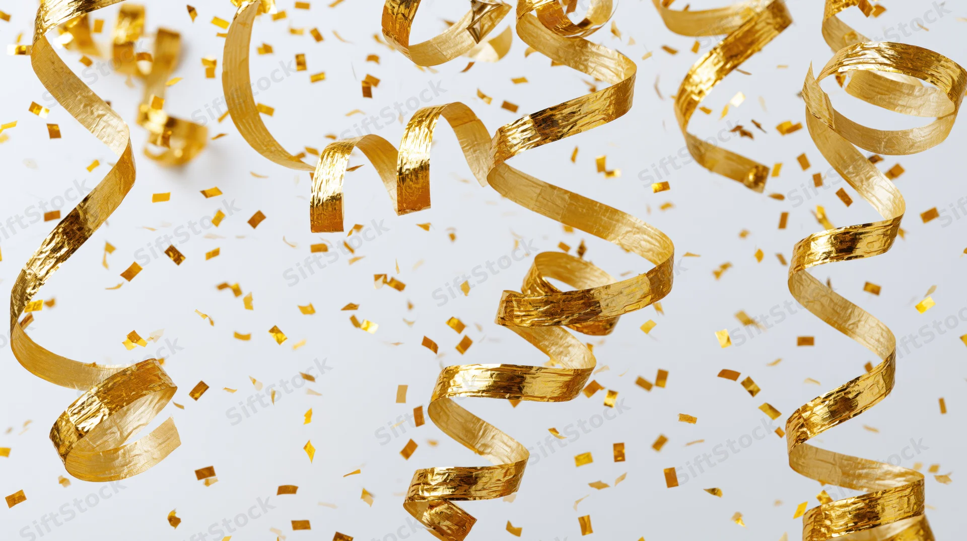 Gold metallic streamers and confetti pieces falling and twisting against a white background