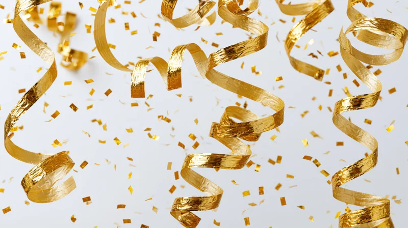 Gold metallic streamers and confetti pieces falling and twisting against a white background