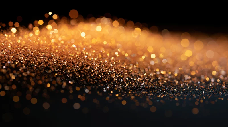 Golden glitter particles scattered across a dark surface with bokeh lights in the background