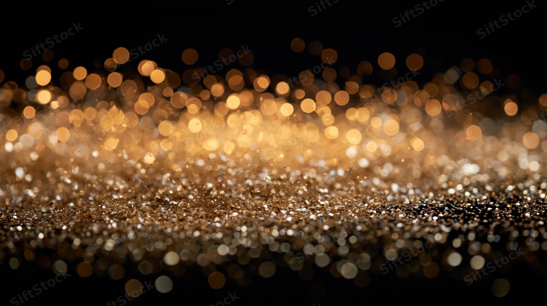 Golden glitter particles scattered across a dark surface with bokeh lights in the background