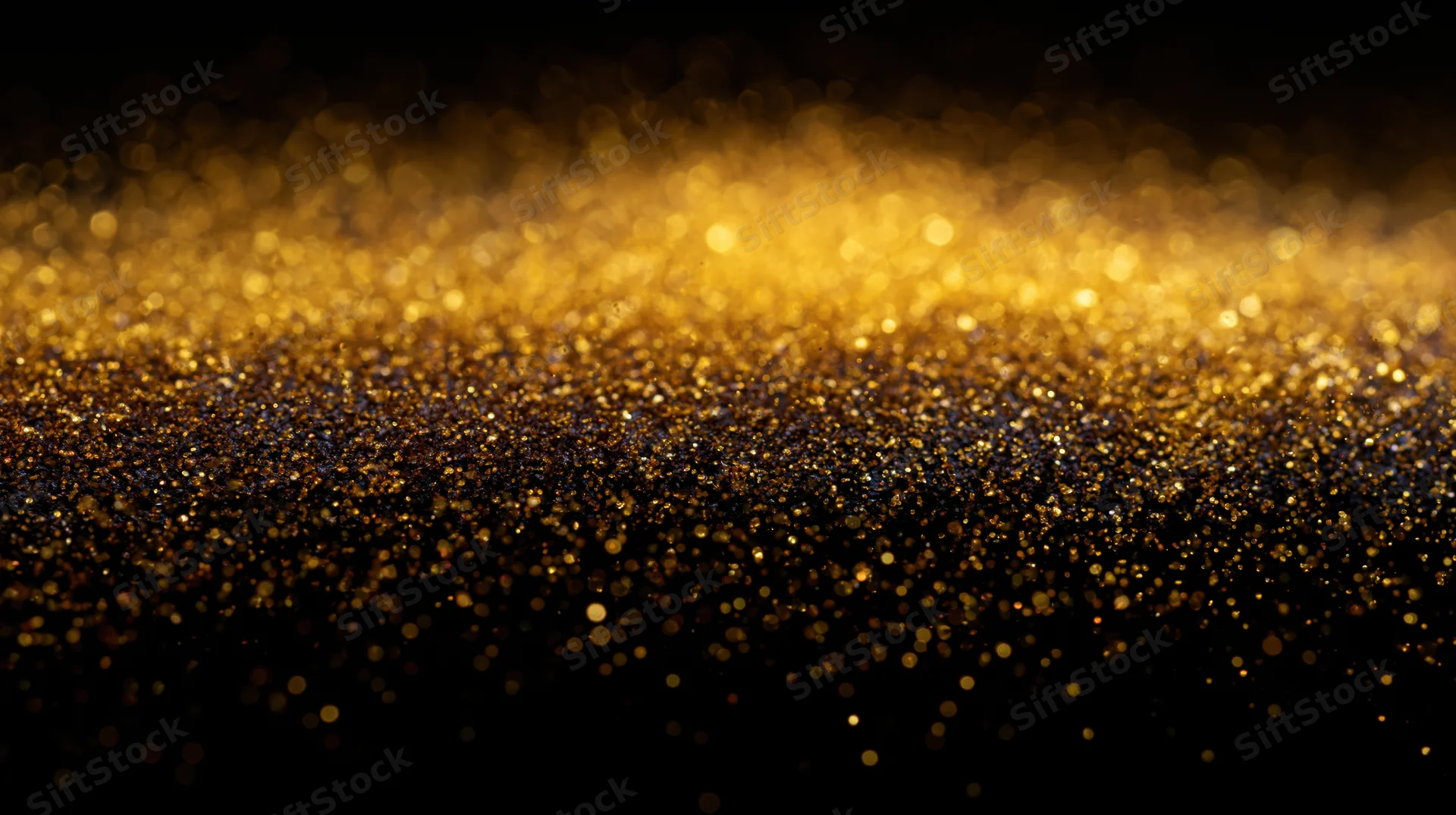 Golden glitter particles scattered across a dark surface creating a shimmering abstract background