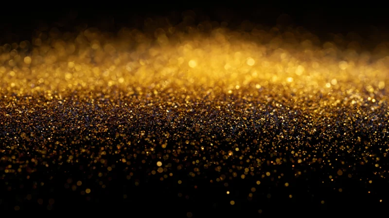 Golden glitter particles scattered across a dark surface creating a shimmering abstract background
